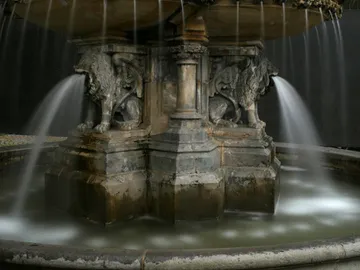 A fountain with lion sculptures splashes water into a pool.