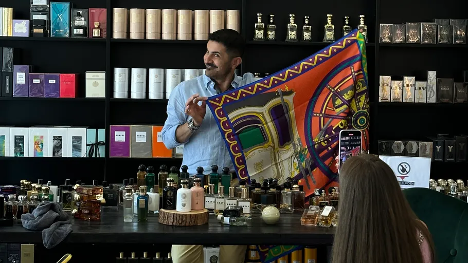 Man displays colorful scarf in perfumery shop.