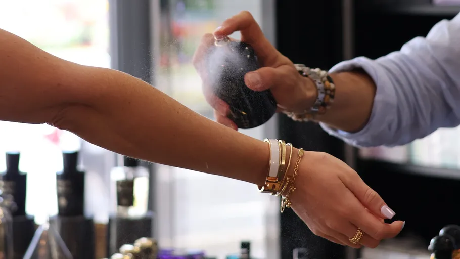 Person spraying perfume on another's wrist indoors.