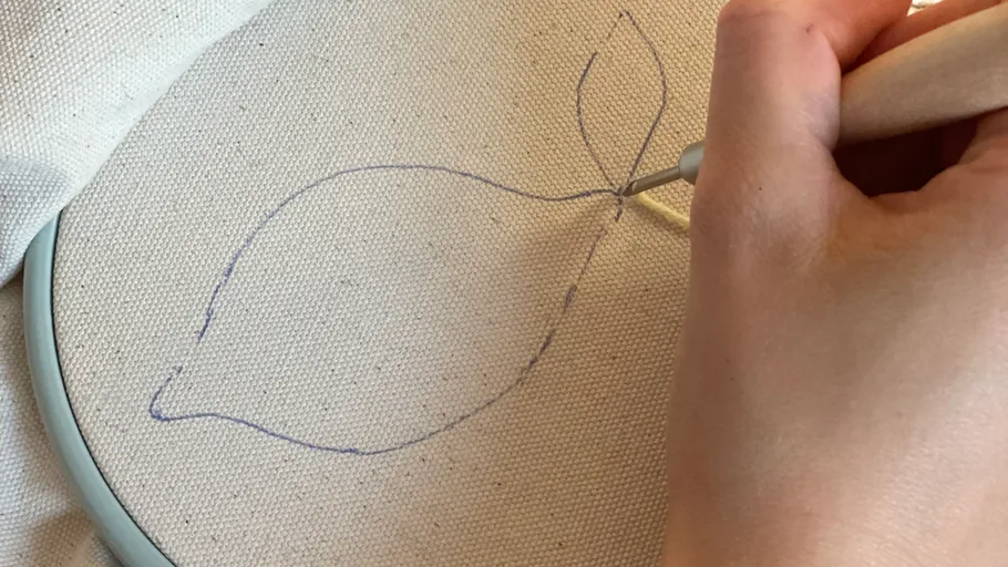 Person mit Stanznadel auf Leinwand mit Blattmuster.
