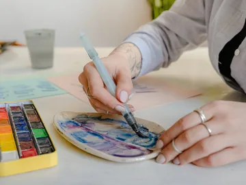 Eine Person malt mit Aquarellfarben auf einer Palette.