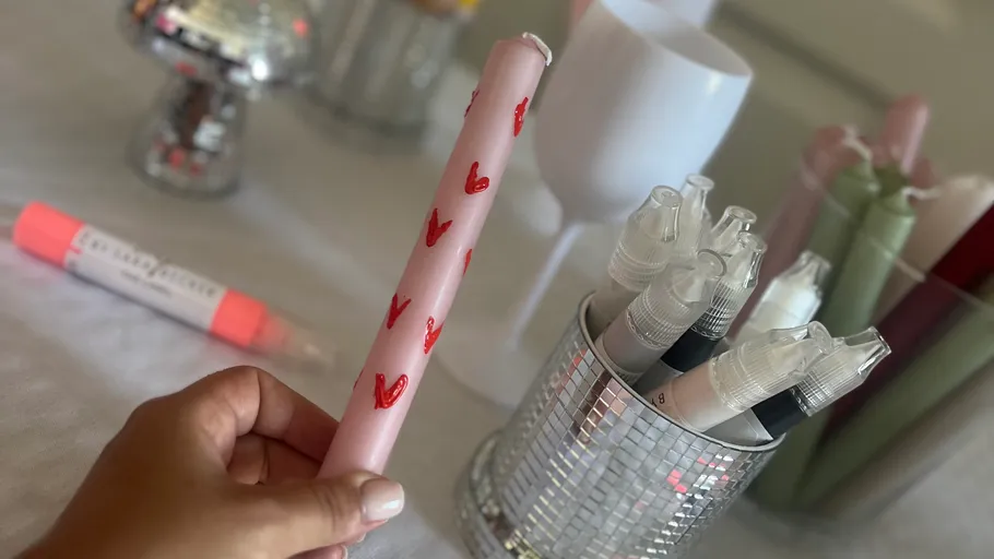 Hand holding candle with red hearts, art supplies nearby.