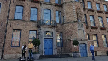 Two people on segways in front of brick building.