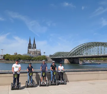 Menschen auf Segways am Fluss mit Domblick.