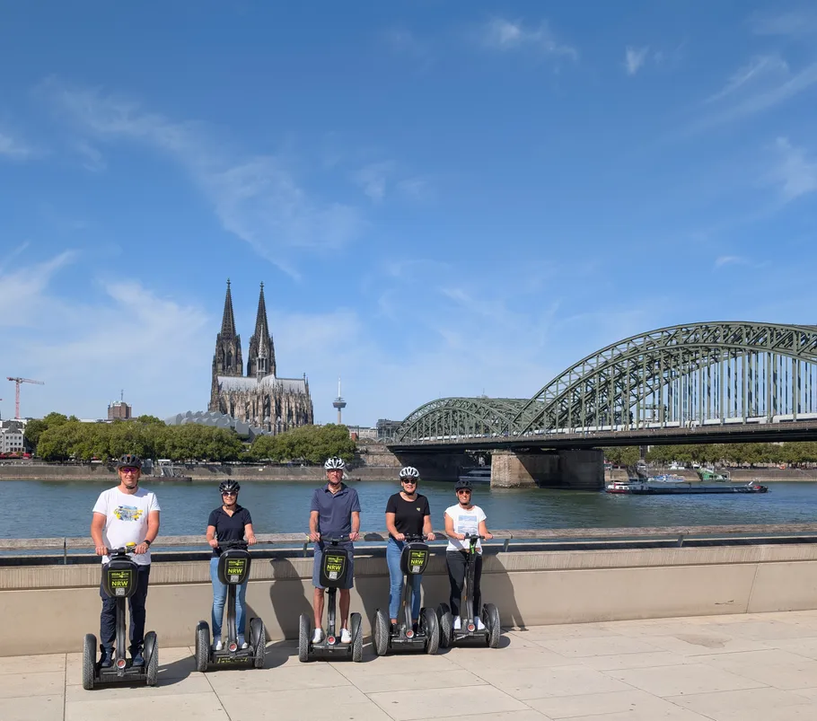 People on segways by river with cathedral view.