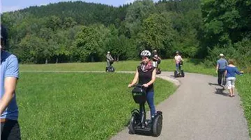 Menschen fahren Segways auf einem Weg mit Bäumen.