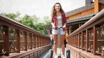 Frau fährt Segway auf Holzbrücke im Freien.
