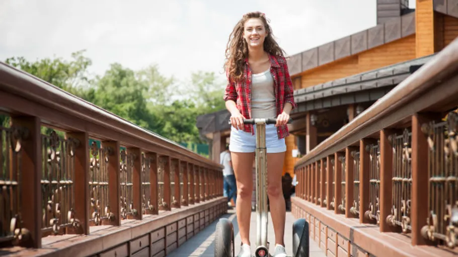 Frau fährt Segway auf Holzbrücke im Freien.
