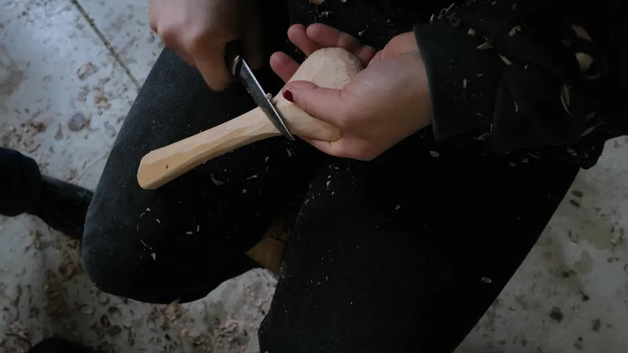 Person carving wooden spoon indoors.