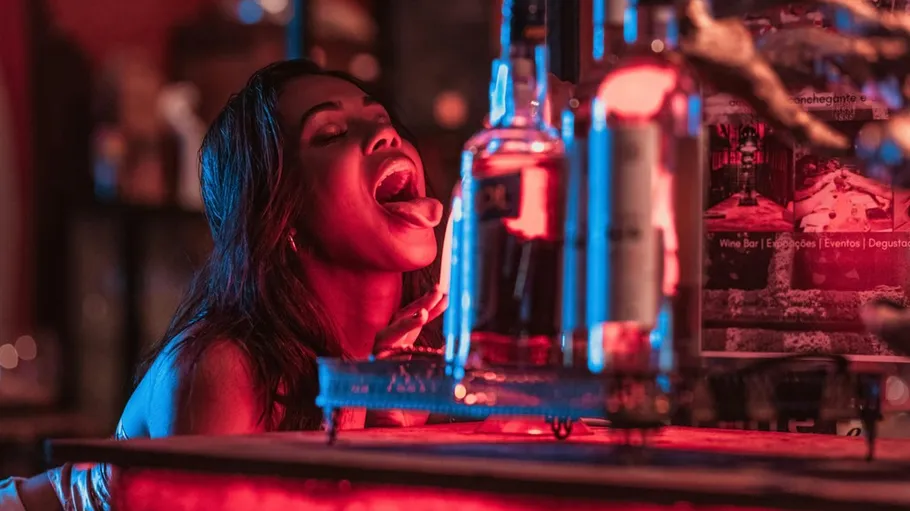 Woman in bar licking a glass bottle.