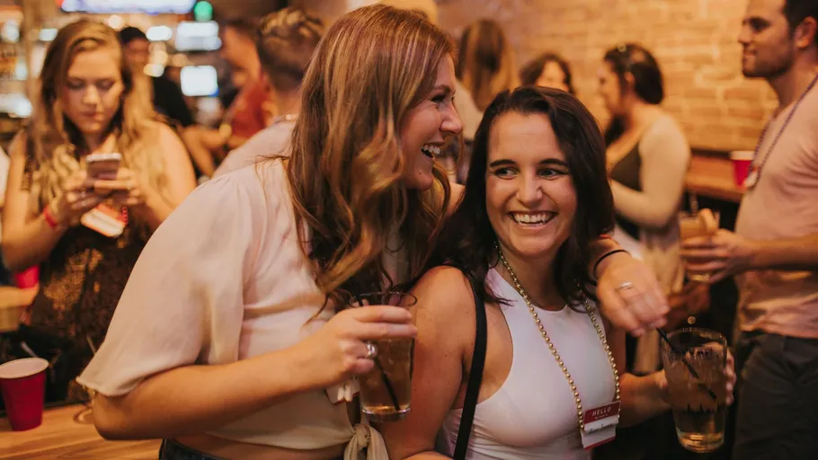 Zwei Frauen lachen auf einer vollen Party.