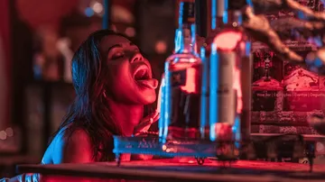 Woman with open mouth near bottles in bar.