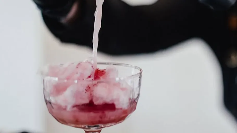 Pouring liquid over pink shaved ice in glass.
