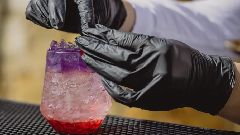 Bartender garnishing vibrant layered cocktail outdoors.