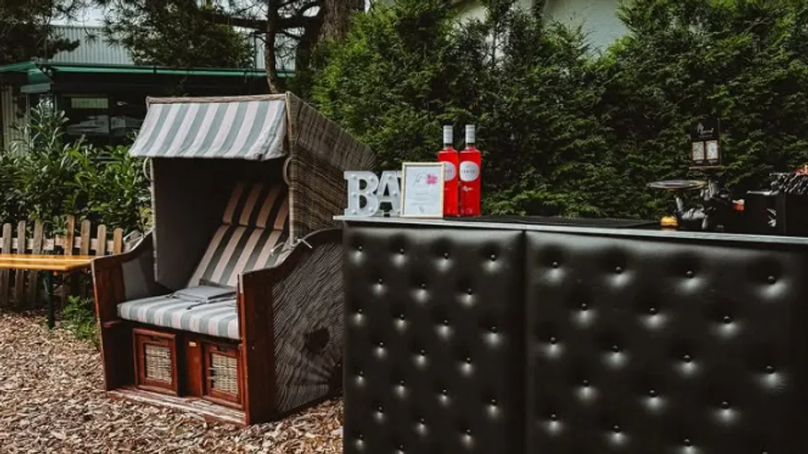 Chair beside outdoor bar with bottles, greenery background.