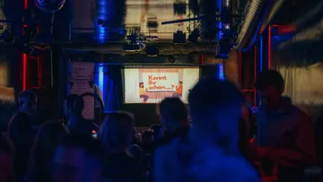 Dark club with people and bright screen.