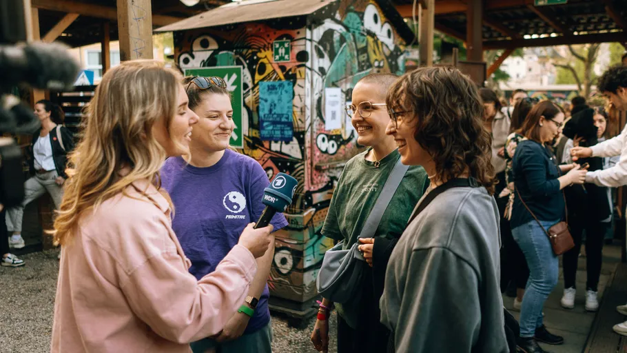 Interviewer speaks with three people outdoors.