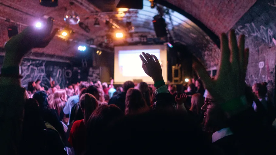 People raising hands in crowded indoor event.