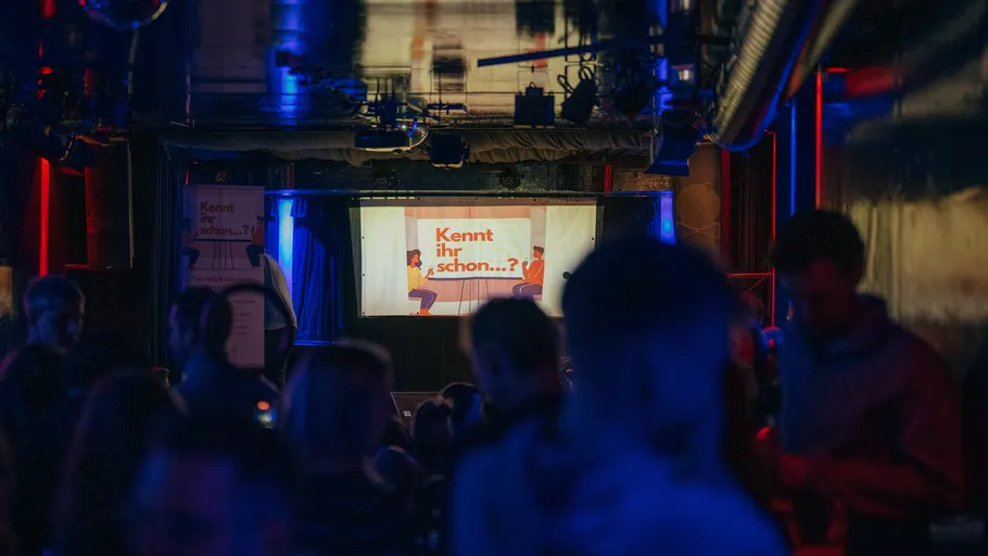 People watching a screen in dimly lit room.