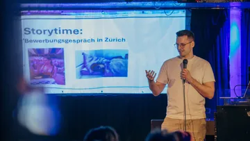 Man with microphone presents beside a projected slide.