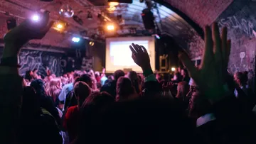 Crowd with raised hands in a dim venue.