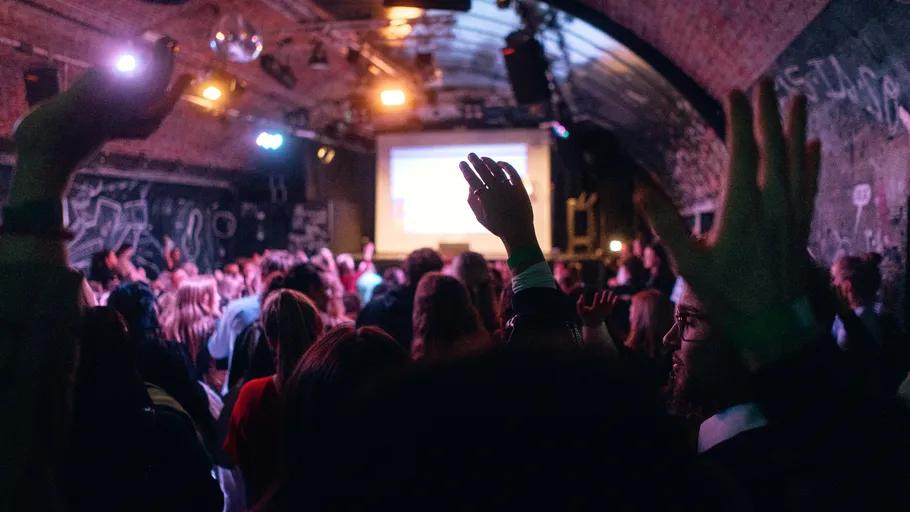 Crowd with raised hands in a dim venue.