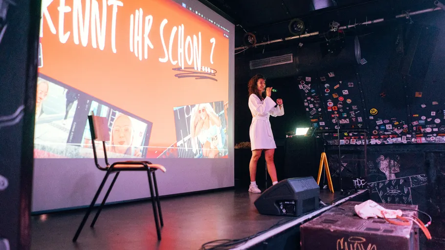Person speaking on stage with presentation screen.