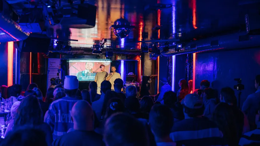 Two people speaking on stage in a club.