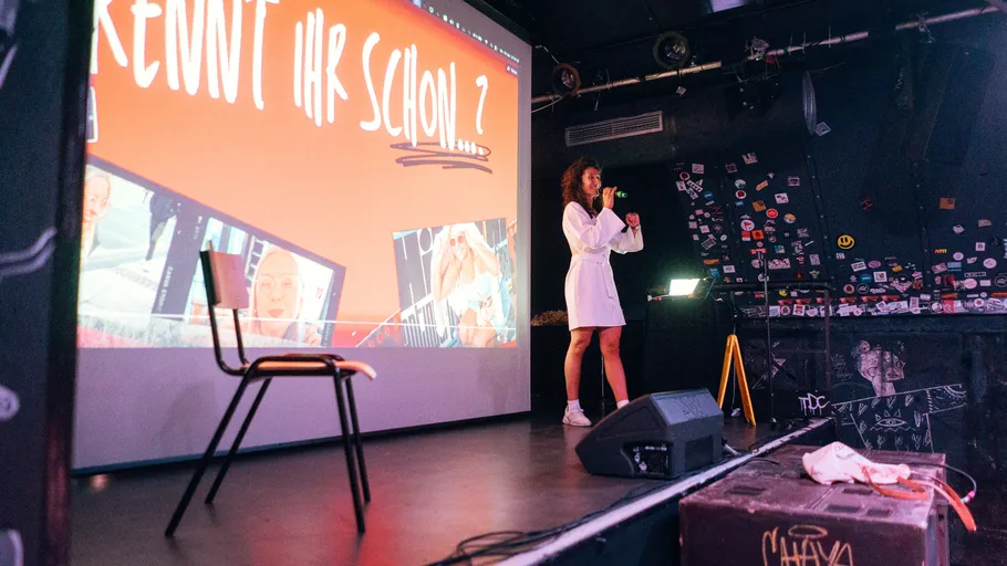 Woman presenting on stage with slideshow.