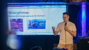 Man presenting with microphone next to screen.