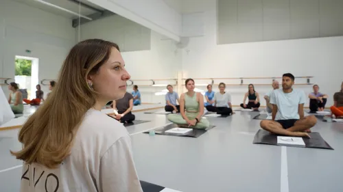 Menschen sitzen im Schneidersitz in einem hellen Studio.