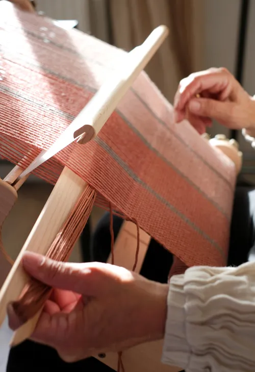 Hands weaving on a wooden loom.