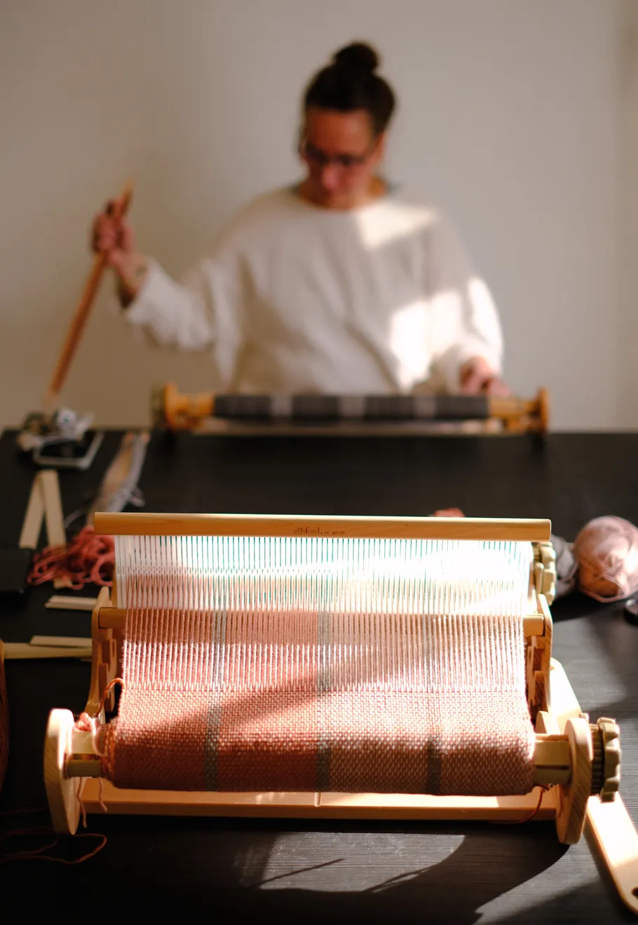 Weaving loom on table, person weaving.