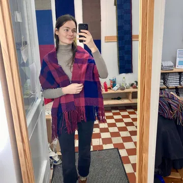 Woman wearing shawl taking mirror selfie indoors.