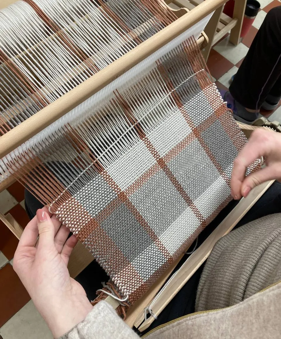 Person weaving on a wooden loom indoors.