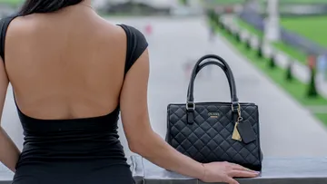 Frau im schwarzen Kleid mit Handtasche draußen.