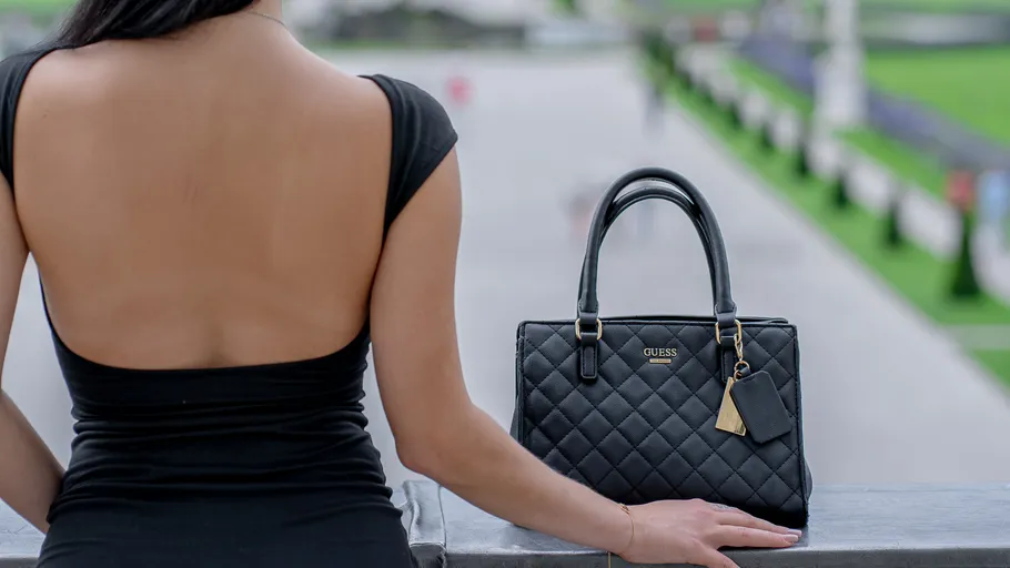 Frau im schwarzen Kleid mit Handtasche draußen.