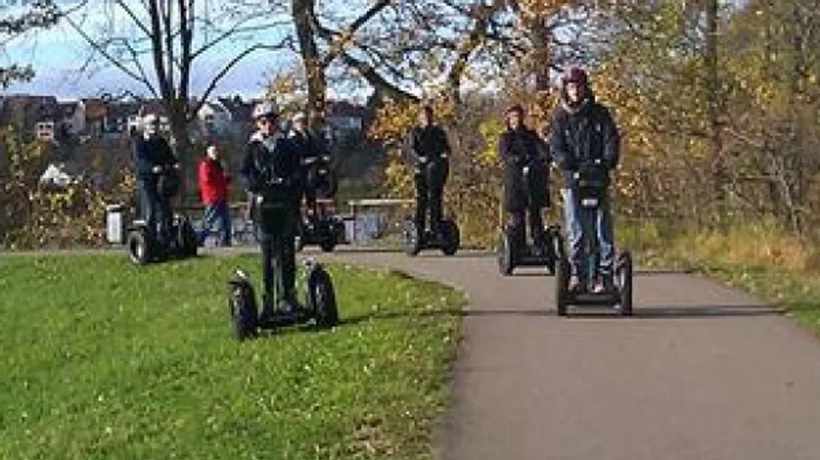 Personen fahren Segways auf einem Parkweg.