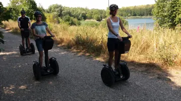 Three people ride segways on a lakeside path.