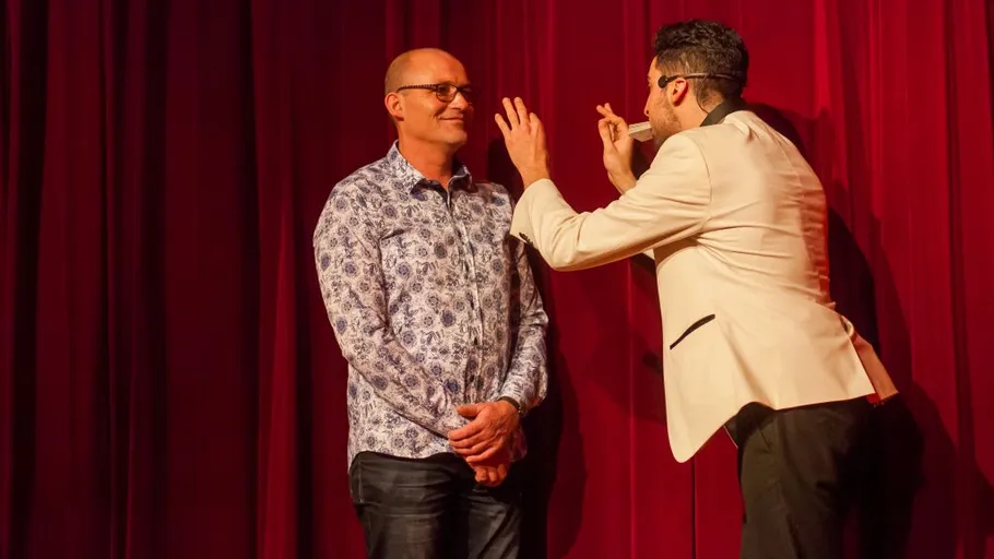 Two men interacting on stage with red curtain.
