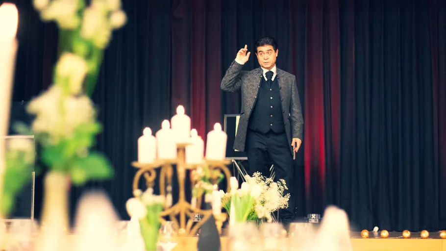 Man in suit gesturing on stage with candles.