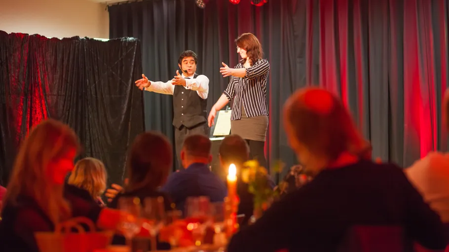 Performer and audience member on stage with curtains.