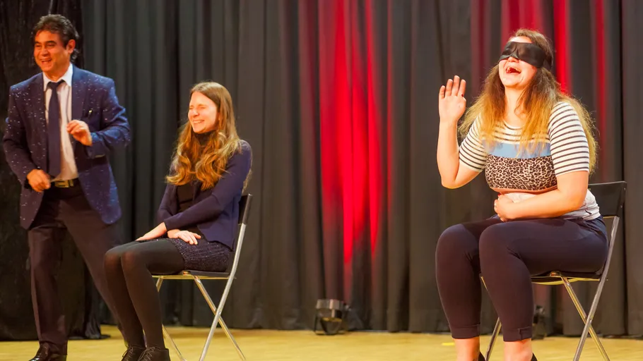 Man and two women on stage, one blindfolded.