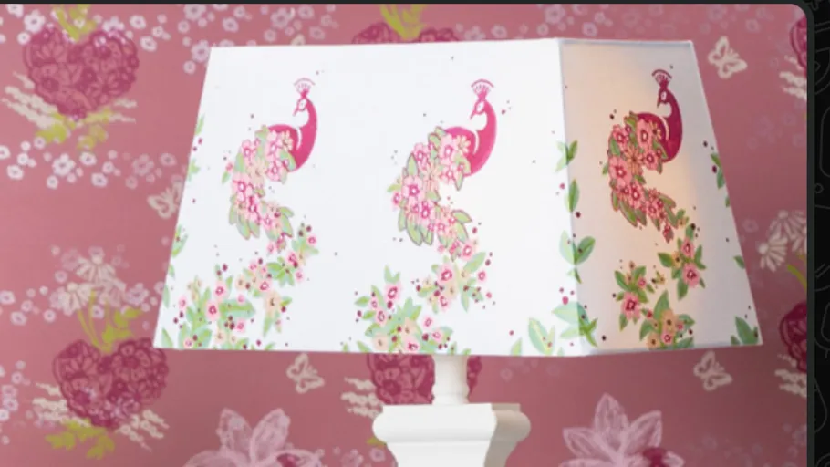 Lampshade with peacock design against floral wallpaper.