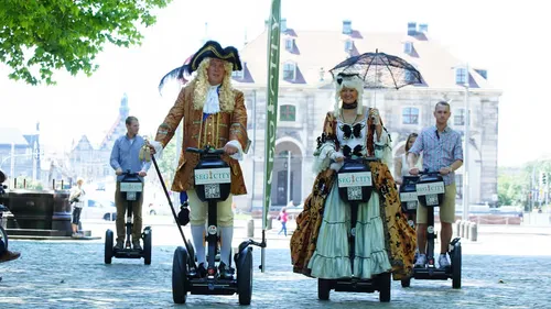 People in historical costumes riding Segways outdoors.