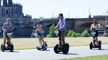 Four people riding Segways near a bridge.