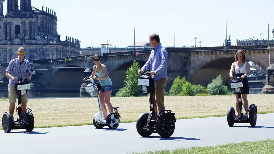 Four people riding Segways near a bridge.