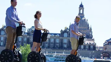 Drei Personen fahren Segways vor historischem Gebäude.