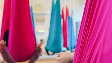 Personen in bunten Yoga-Hängematten drinnen.