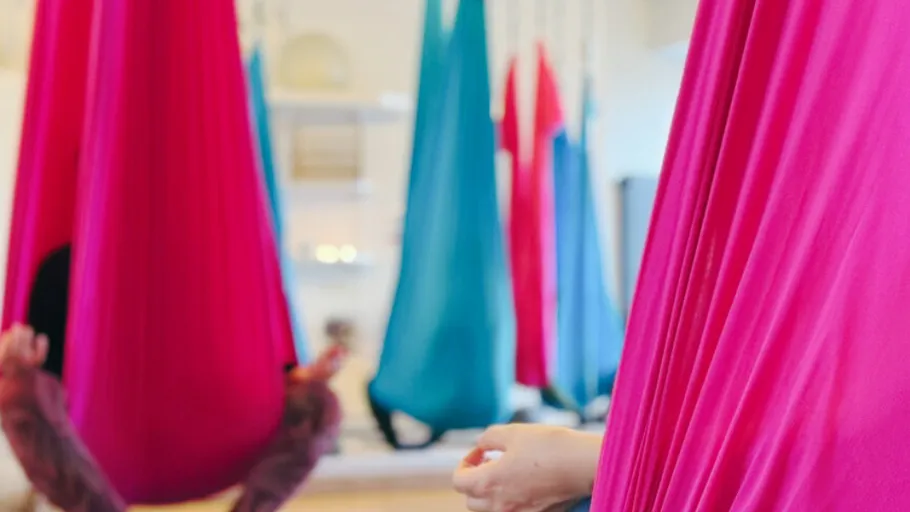 People in colorful aerial yoga hammocks indoors.